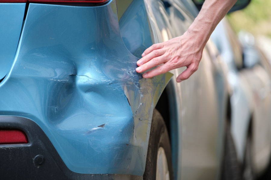 driver-hand-examining-dented-car-with-damaged-fender